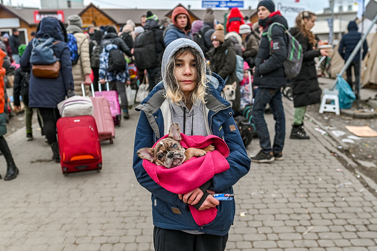 A young Ukrainian refugee carries her beloved dog in her arms as she waits at the Ukrainian Polish border in Medyka, Poland. Forced to flee her home with only what she could carry, she chose her dog. Poland, 2022. Miloš Bičanski / We Animals