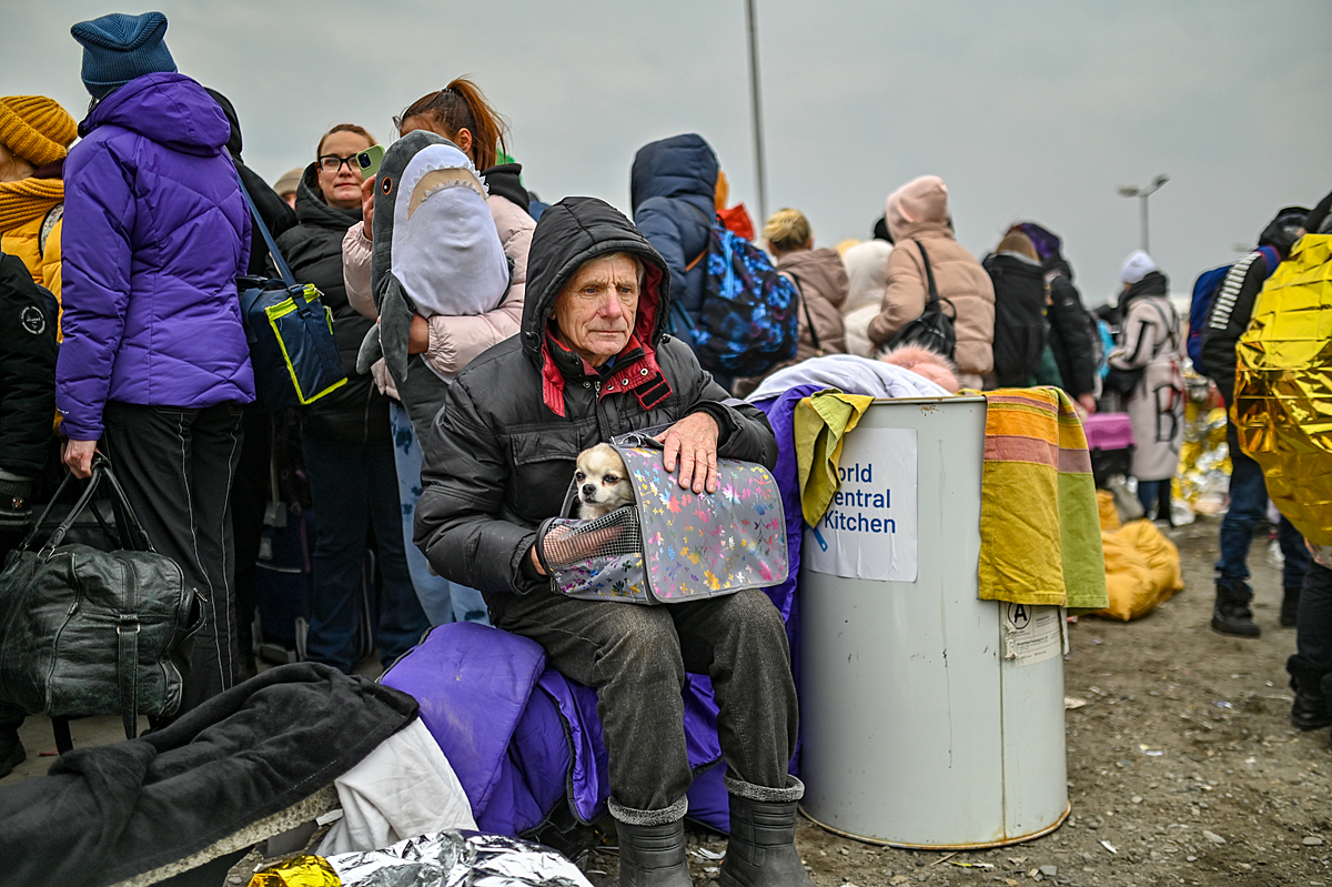 A man sits with his small dog on his lap at the reception center in Medyka on the Polish Ukrainian Border. The Ukrainian refugee is cold, hungry and exhausted after fleeing his home with only what he could carry. Poland, 2022. Miloš Bičanski / We Animals