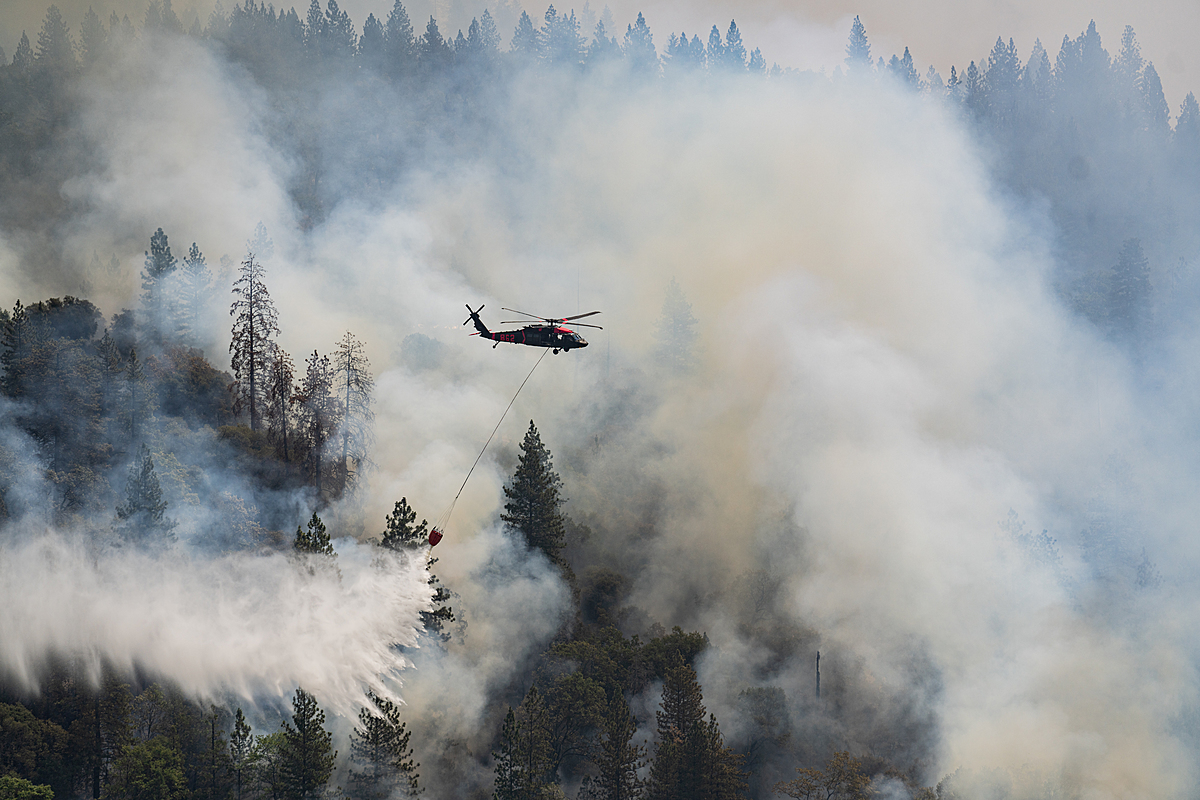 Helicopters work continually throughout the day dropping water on a hot zone that erupted near the fire decimated town of Grizzly Flats, CA. USA, 2021. Nikki Ritcher / We Animals